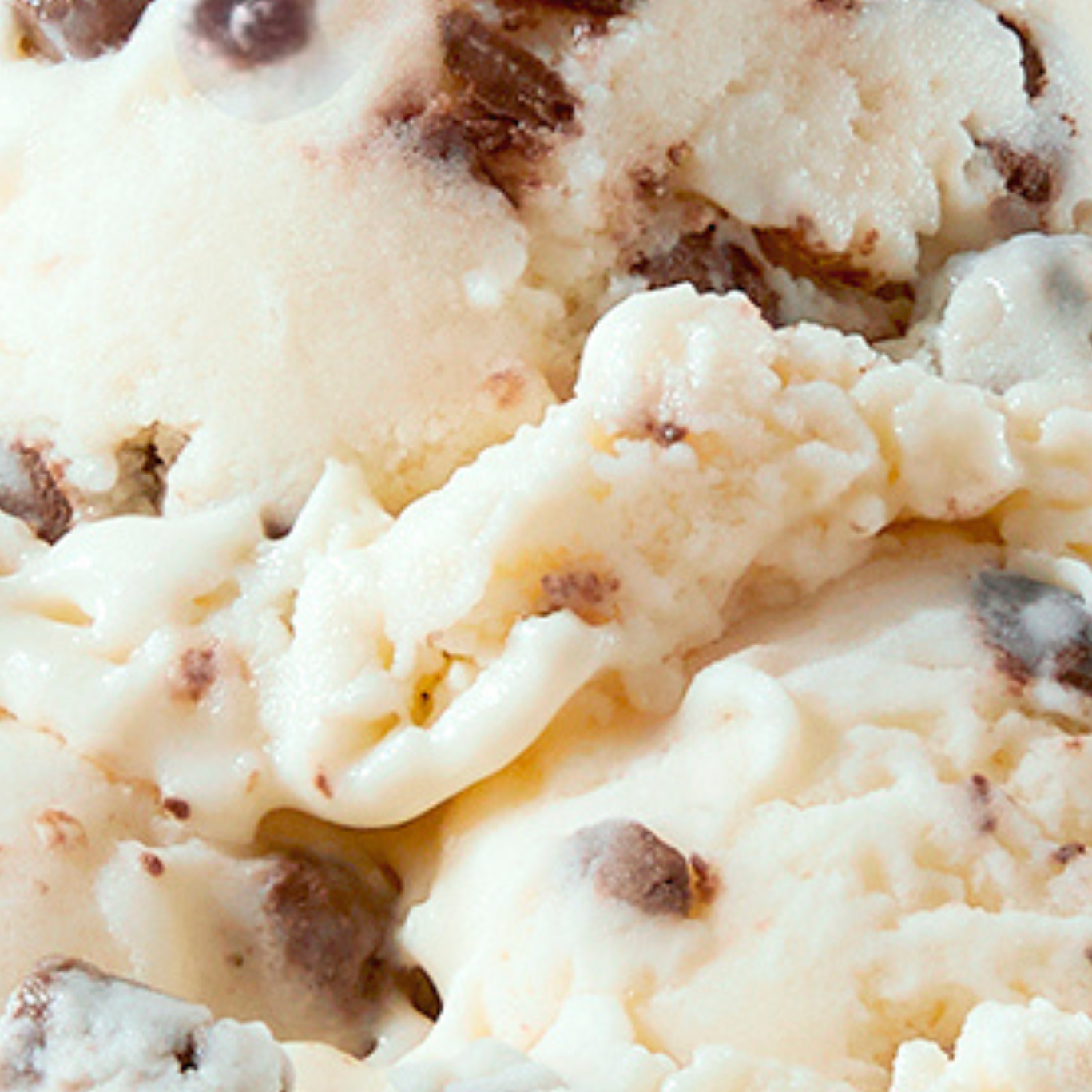 Close-up of a scoop of N!CK'S Cheesecake Brownie light ice cream in a bowl, clearly showing the creamy vanilla base with visible bits of cheesecake and brownie swirl.