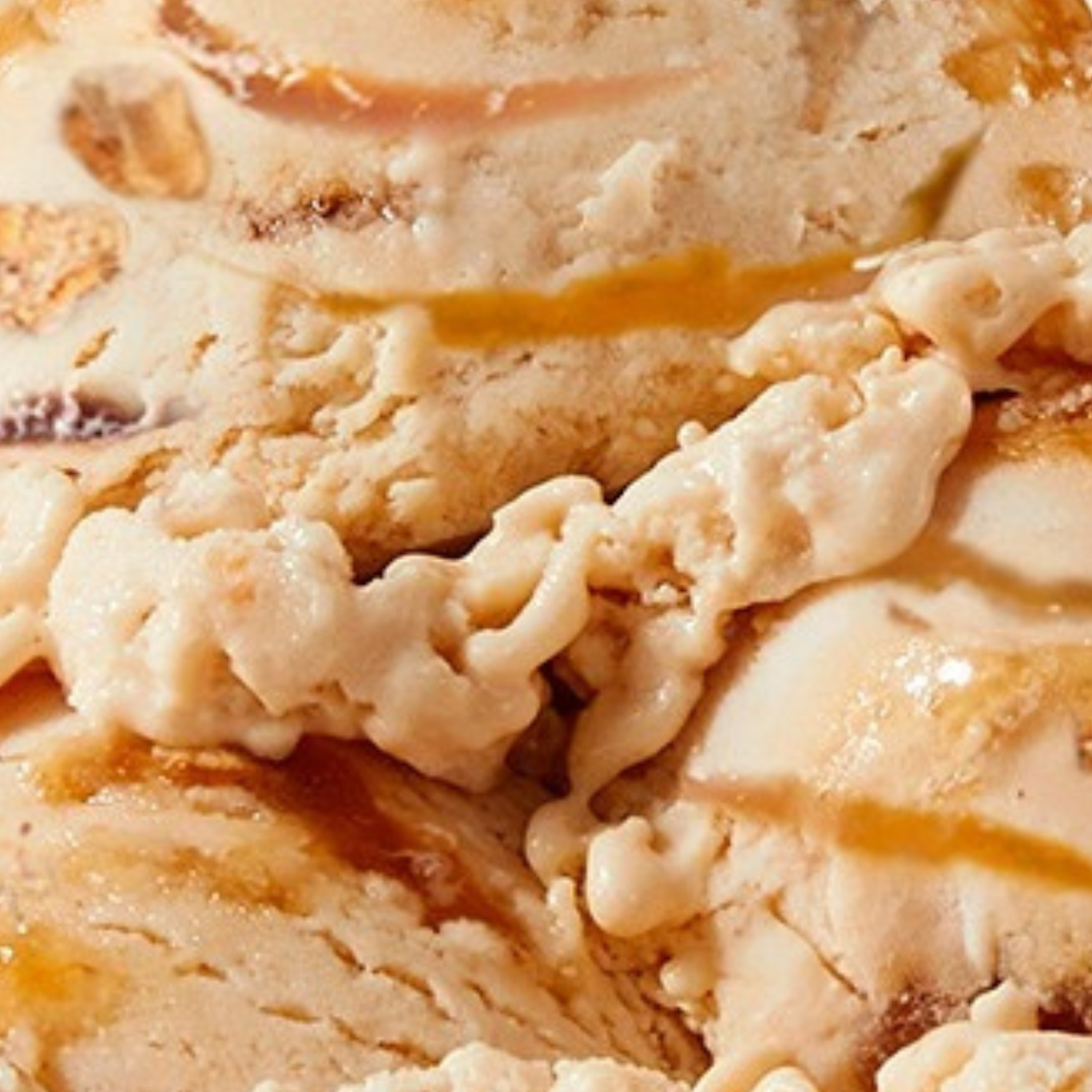 Extreme close-up texture shot of N!CK'S Peanut Caramel Crunch light ice cream, showing light caramel-colored ice cream with crunchy peanut pieces and rich caramel swirls.