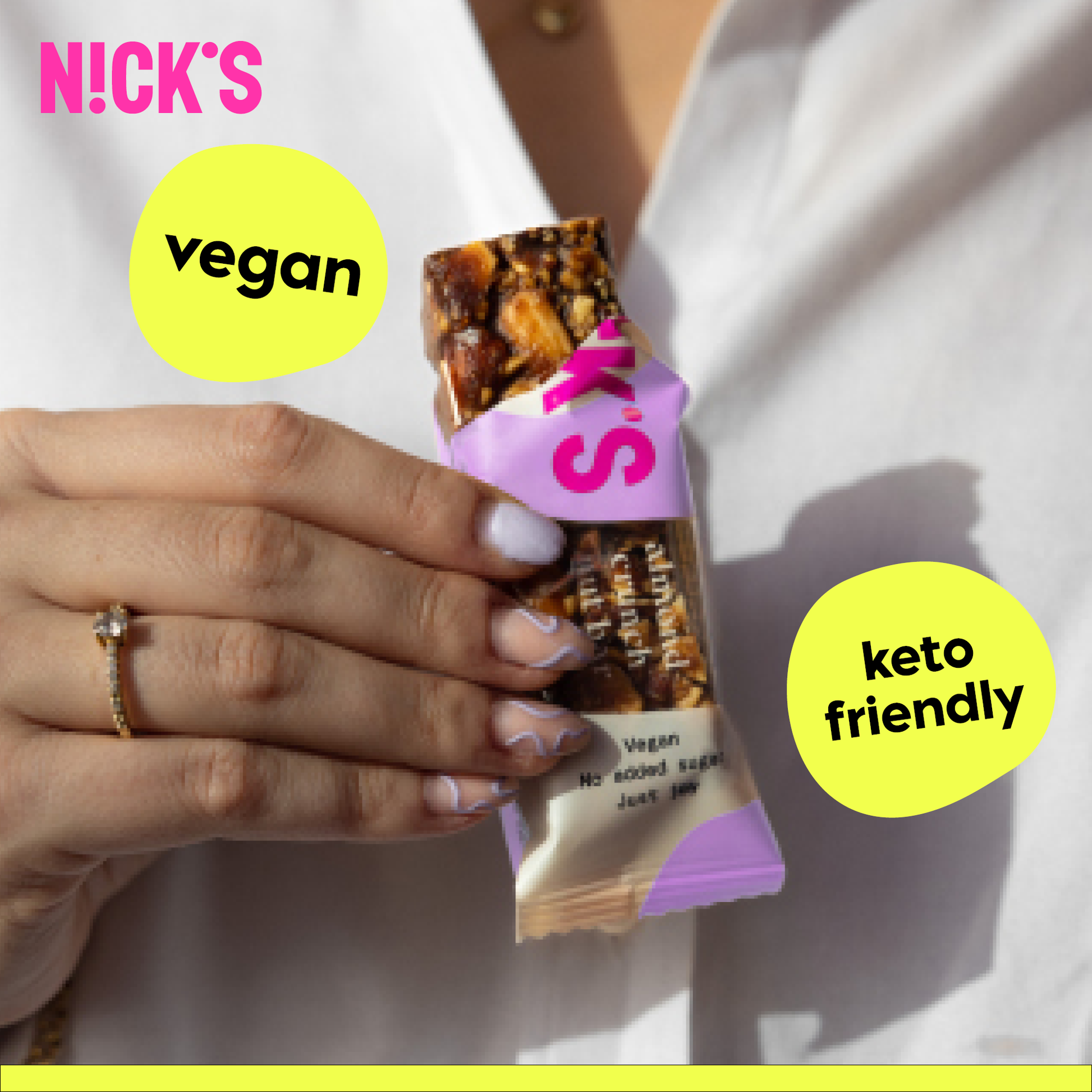 Close-up of a hand with painted nails holding a N!CK'S Almond Crunch Nut Bar. Text highlights 'vegan' and 'keto friendly' features of the snack.